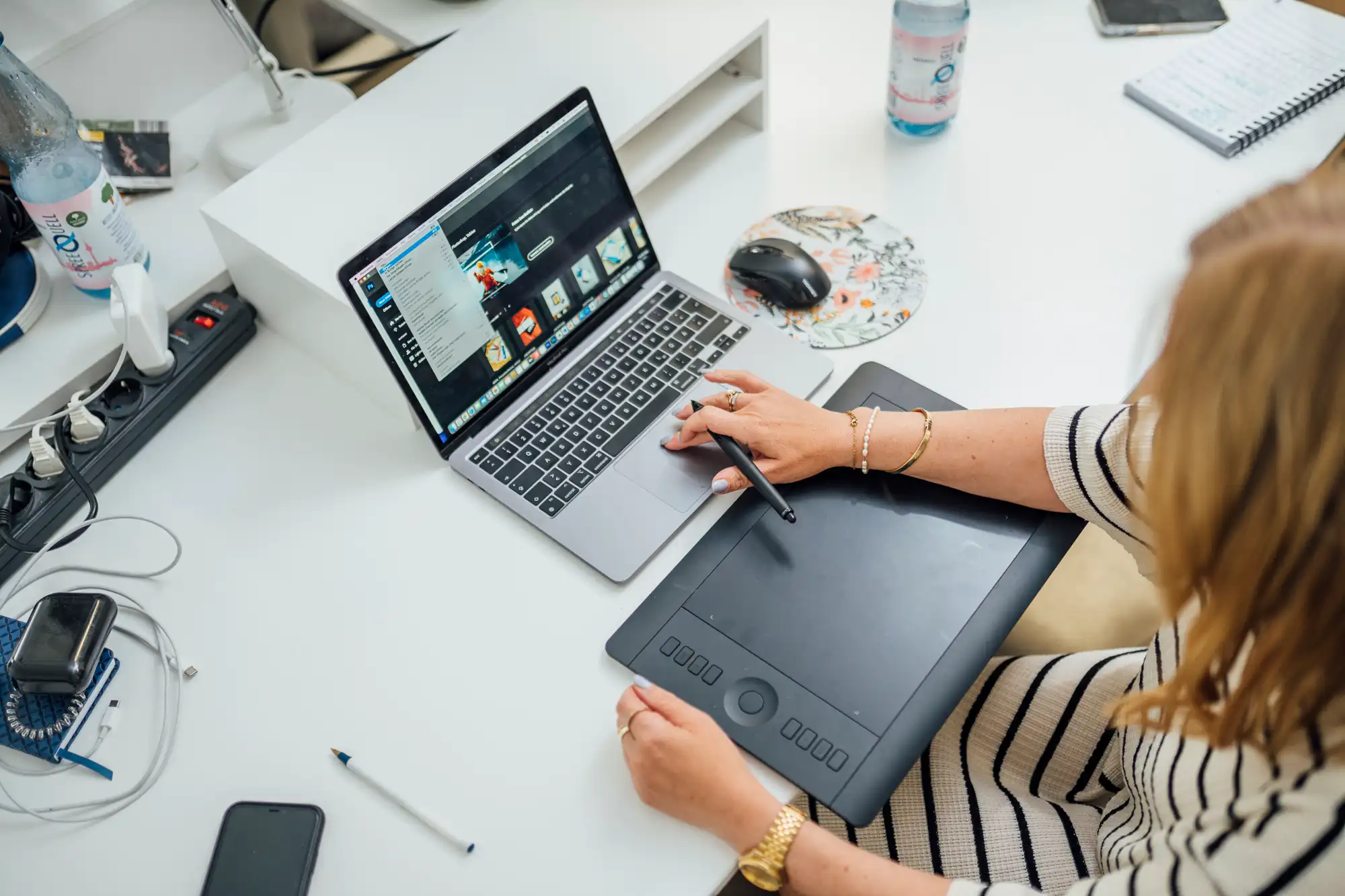 Eine Mitarbeiterin gestaltet Inhalte mit Laptop und Grafiktablett.